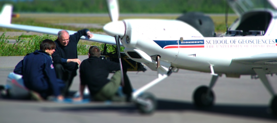 Three people under a light aircraft wing doing maintenance work