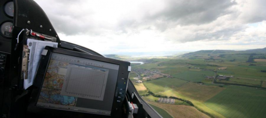 View from an airplane cockpit in flight overlooking green mountains, with a cockpit instrumental panel in the shot